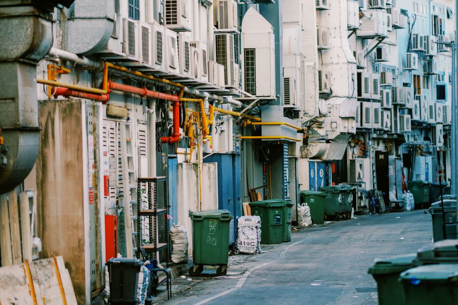 A narrow alleyway situated between two brick buildings, with a dark awning overhead. On the left wall, there is a red and white clearance height sign indicating 11 feet 0 inches, and adjacent to it ar